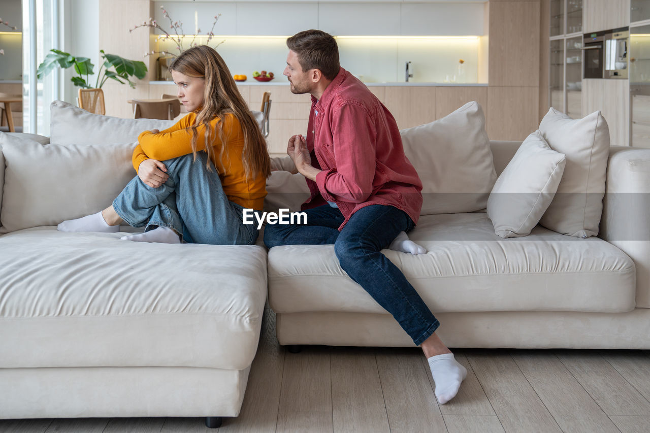 young woman using phone while sitting on bed at home