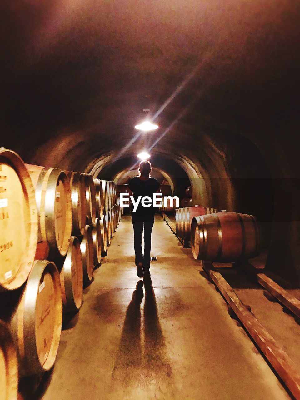 REAR VIEW OF MAN STANDING IN ILLUMINATED PARK