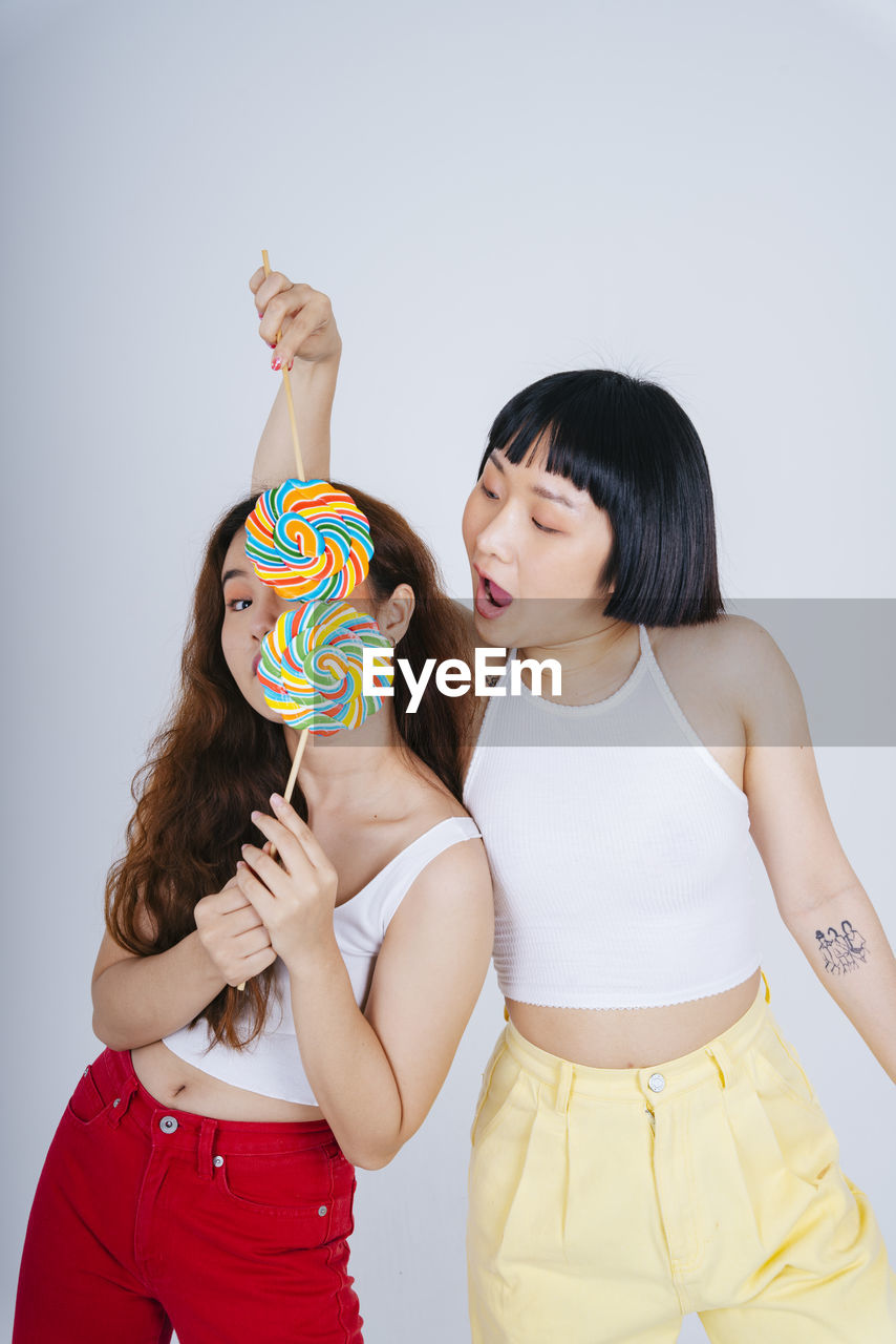 Lesbian couple holding lollipop against white background