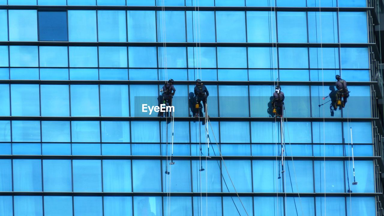 LOW ANGLE VIEW OF PEOPLE WORKING ON GLASS BUILDING