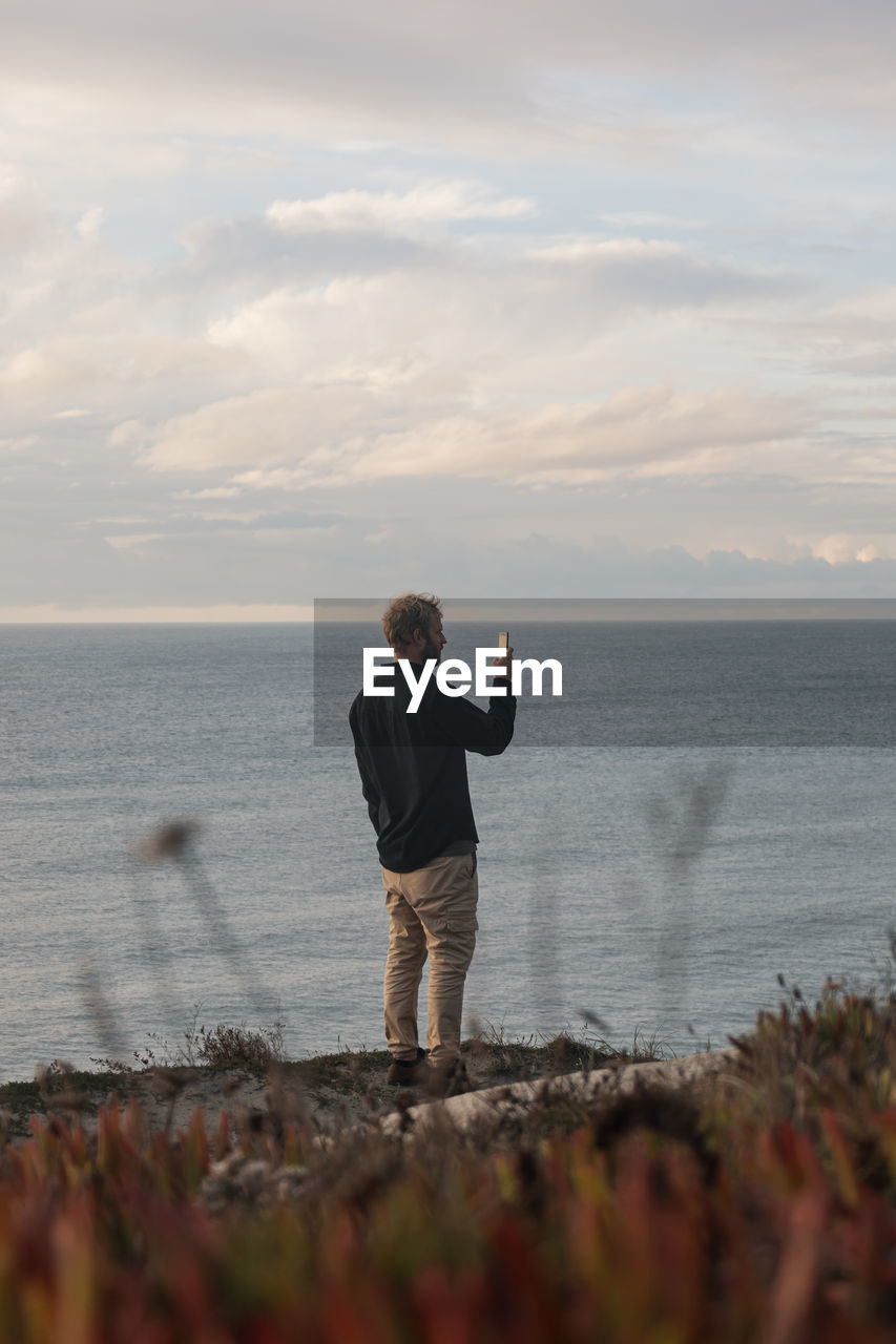 Rear view of man standing on beach against sky