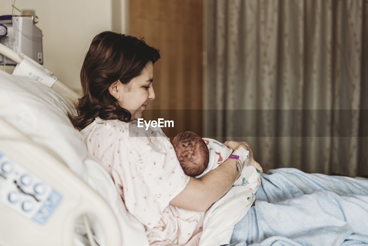 Side view of happy mother holding newborn son in hospital