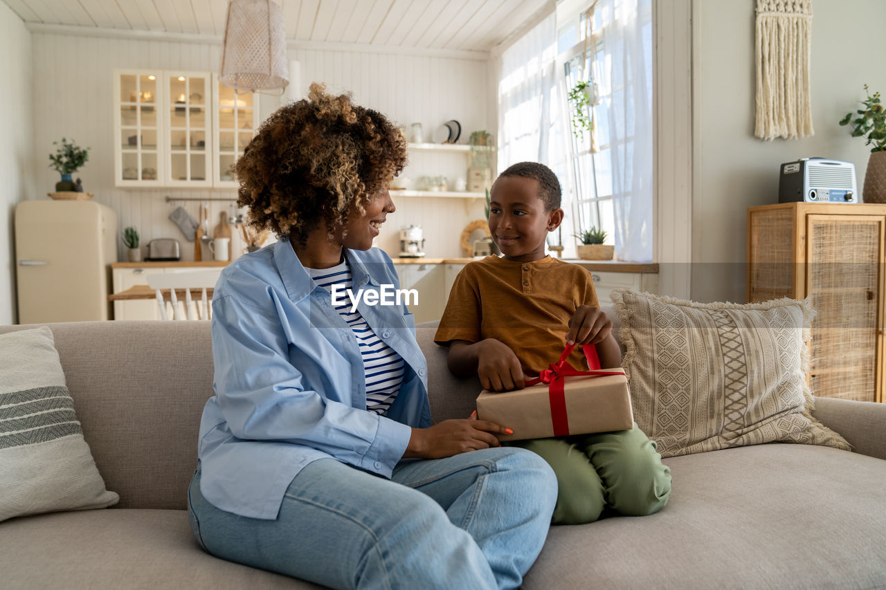 Smiling excited mother receiving birthday gift from son at home