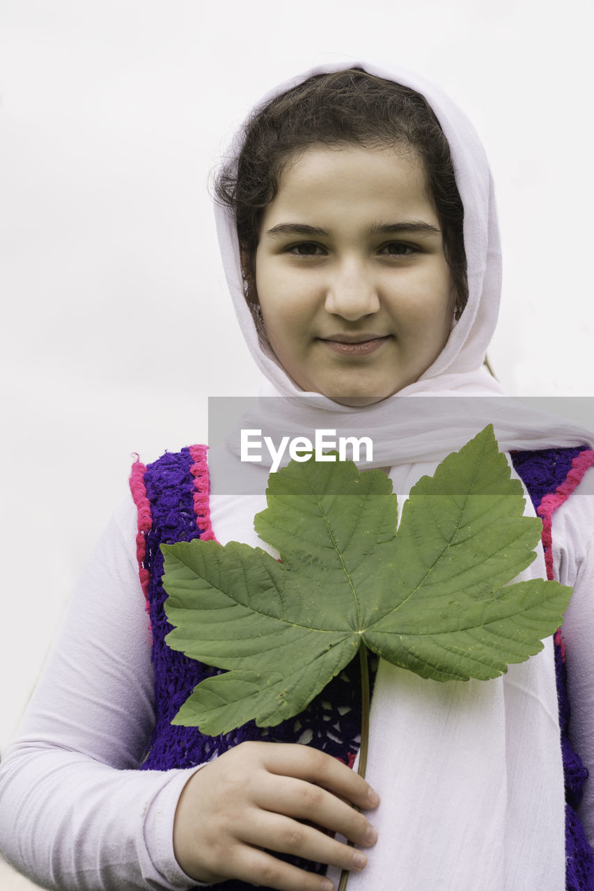 Portrait of smiling girl holding leaf while against white background