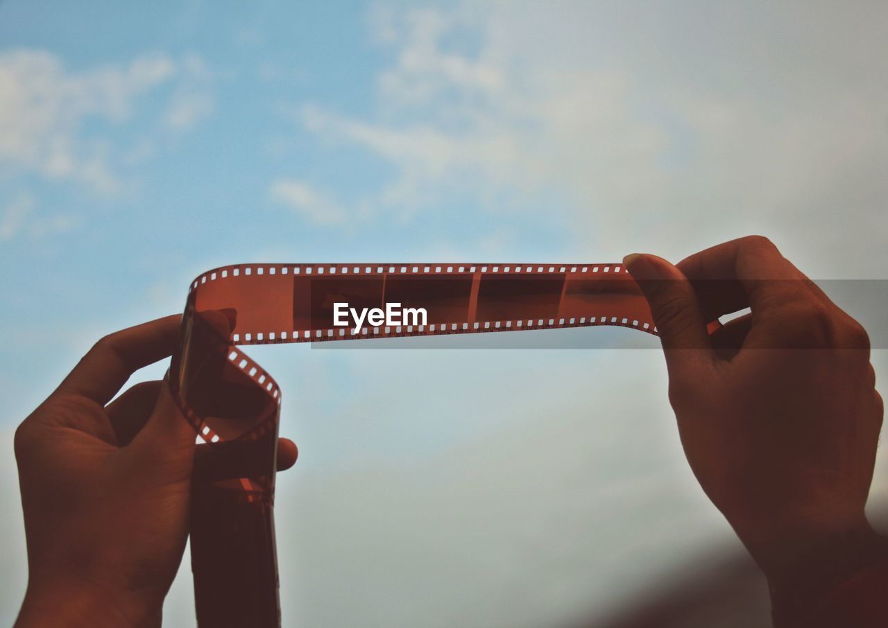 Close-up of hand holding camera reel against sky