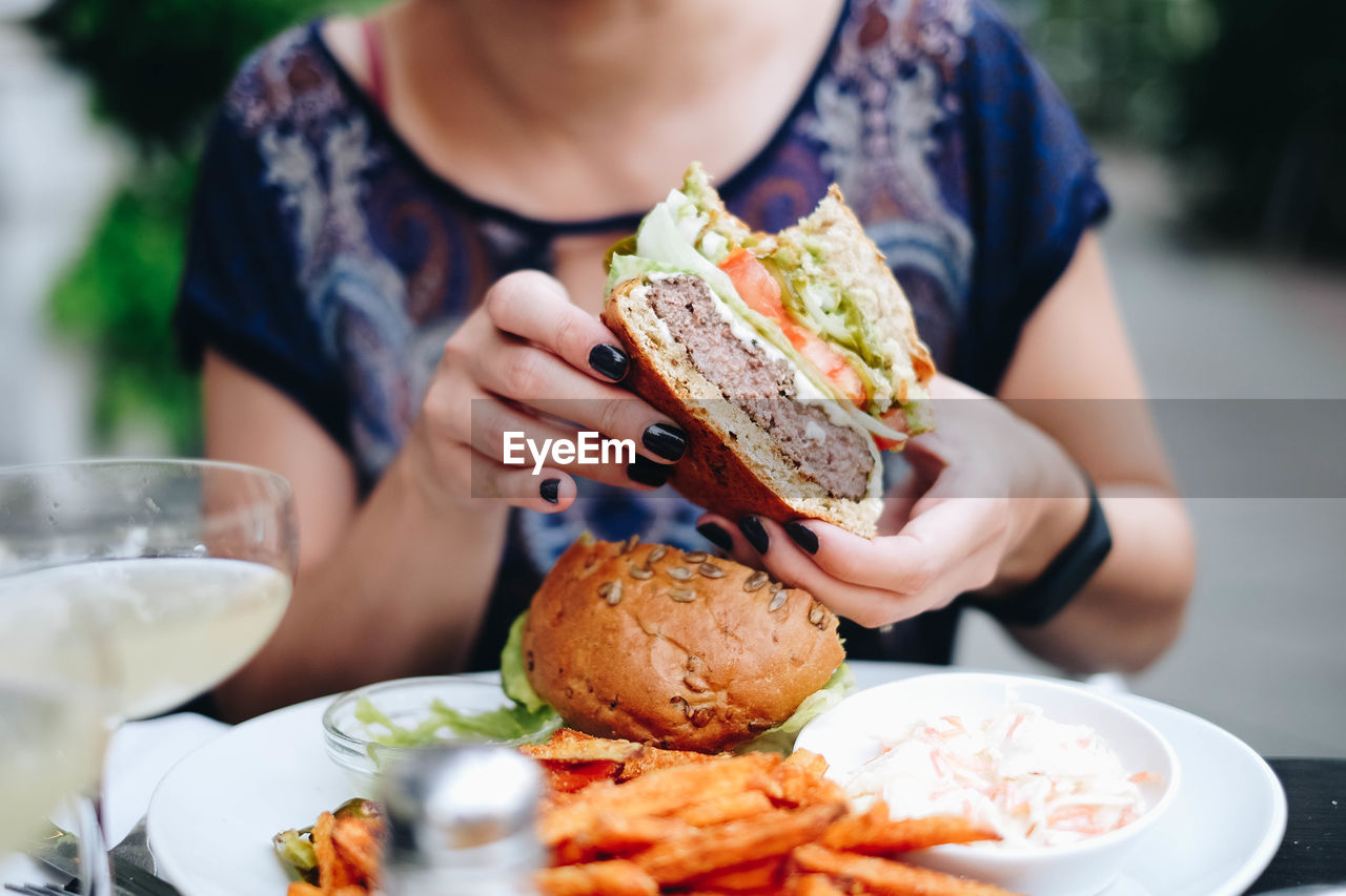 Midsection of woman holding having burger at restaurant