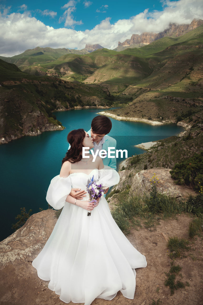 Beautiful couple kisses and hugs against the background of a mountain river and an epic sky. wedding