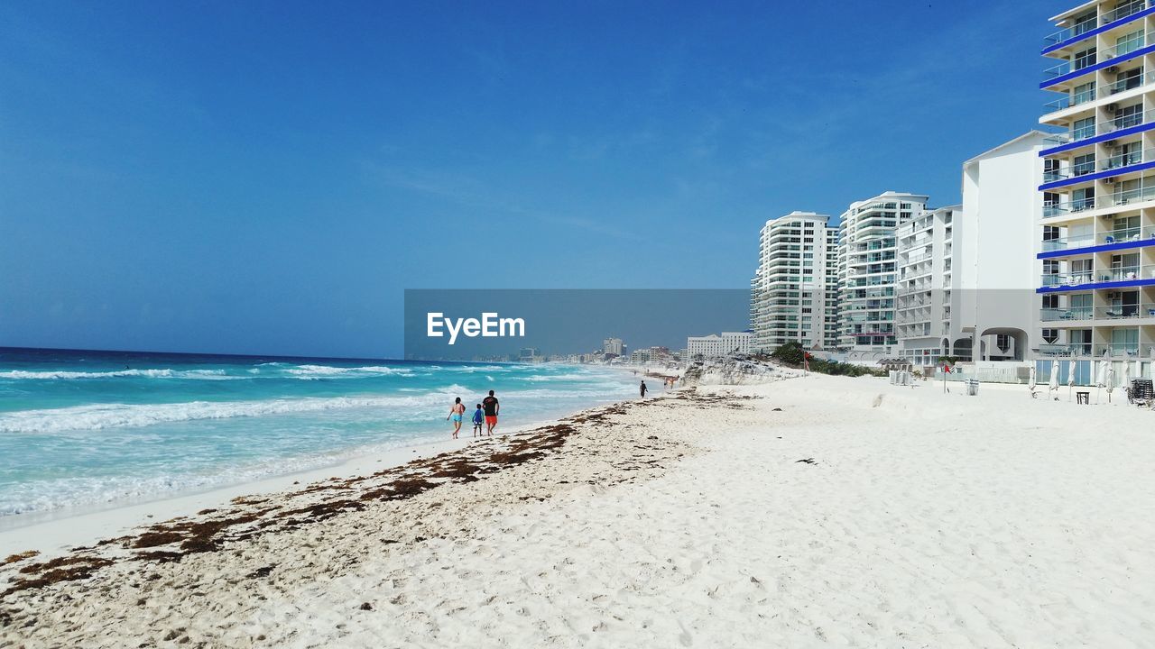 People on beach against clear blue sky in city