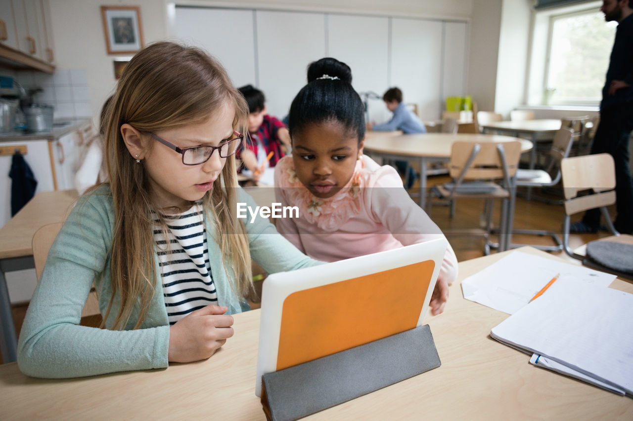 Serious students looking at digital tablet while sitting in classroom