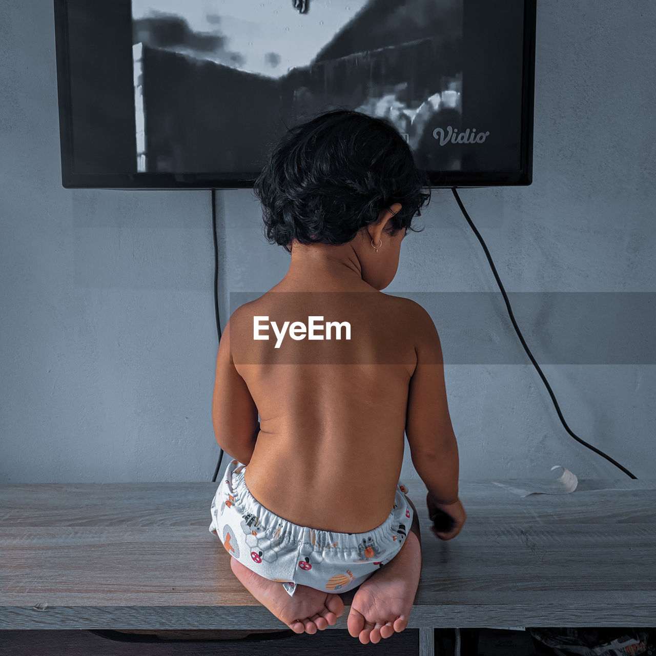 REAR VIEW OF SHIRTLESS BOY LOOKING THROUGH WALL