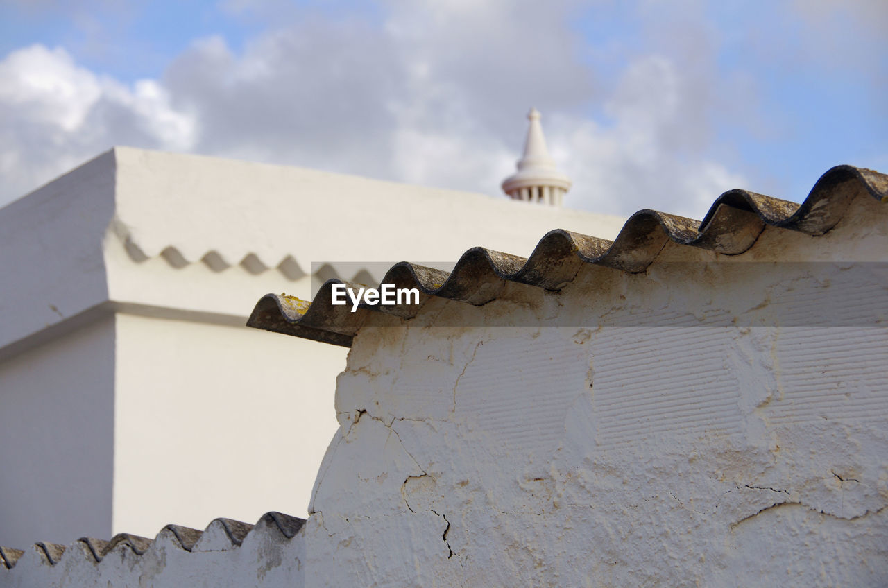 A close up view of a white wall and a tiled roof with a chimney at the background, in portugal
