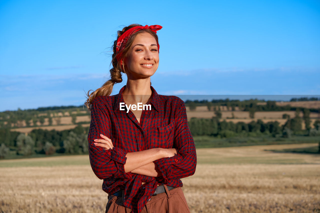 PORTRAIT OF SMILING YOUNG WOMAN STANDING ON FIELD