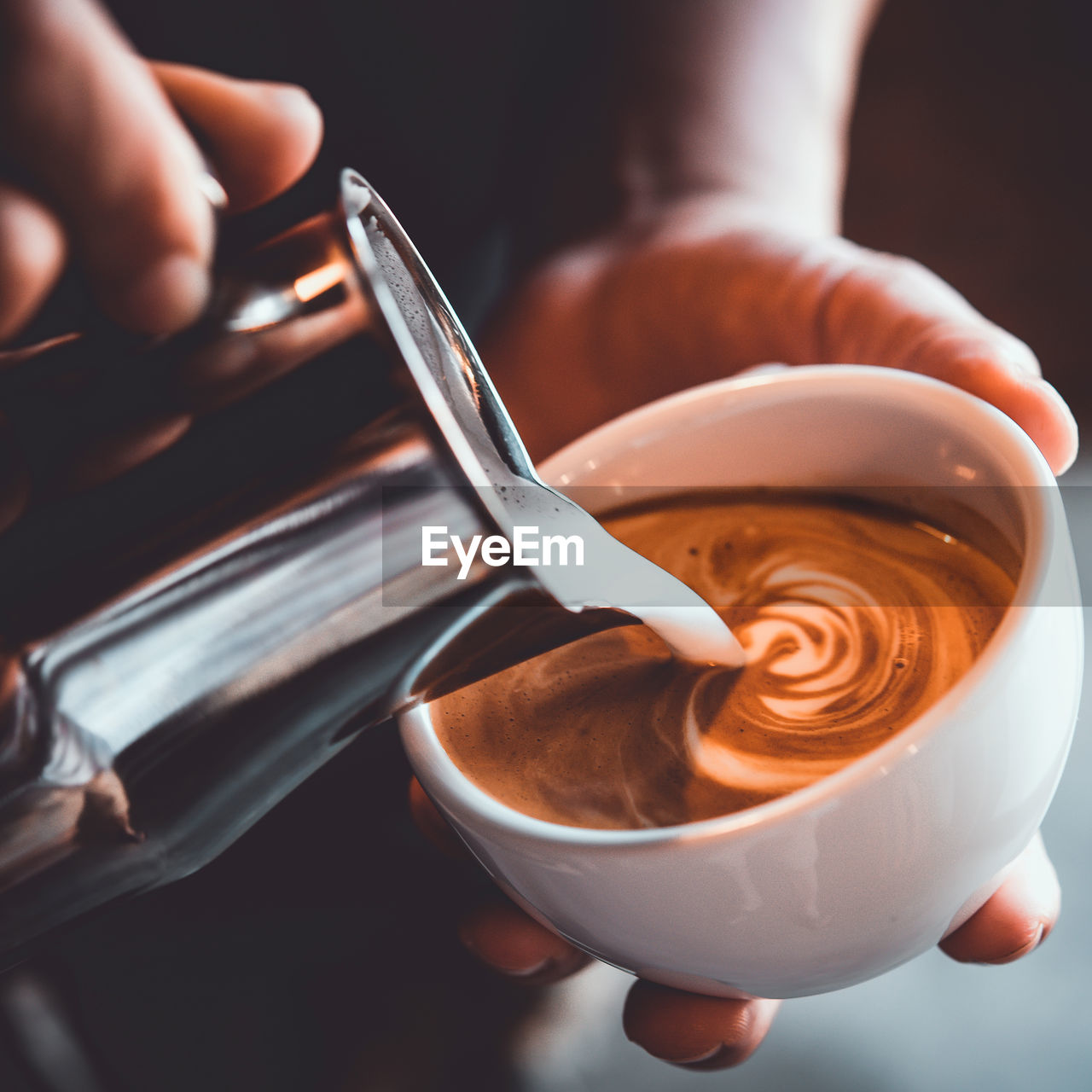 Midsection of person pouring milk in coffee cup