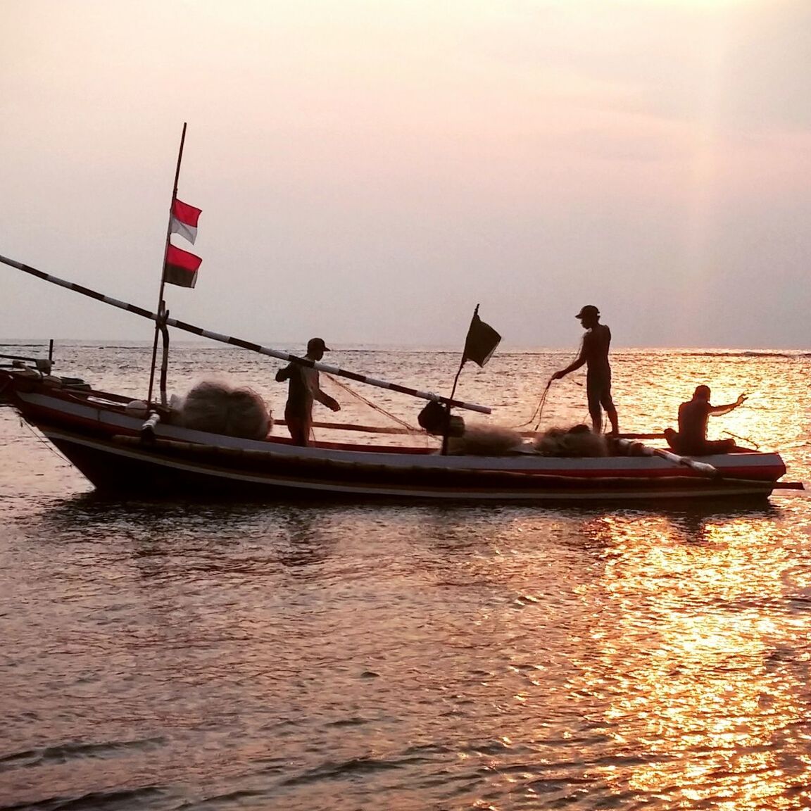 Silhouette fishermen on boat holding fishing net at sea
