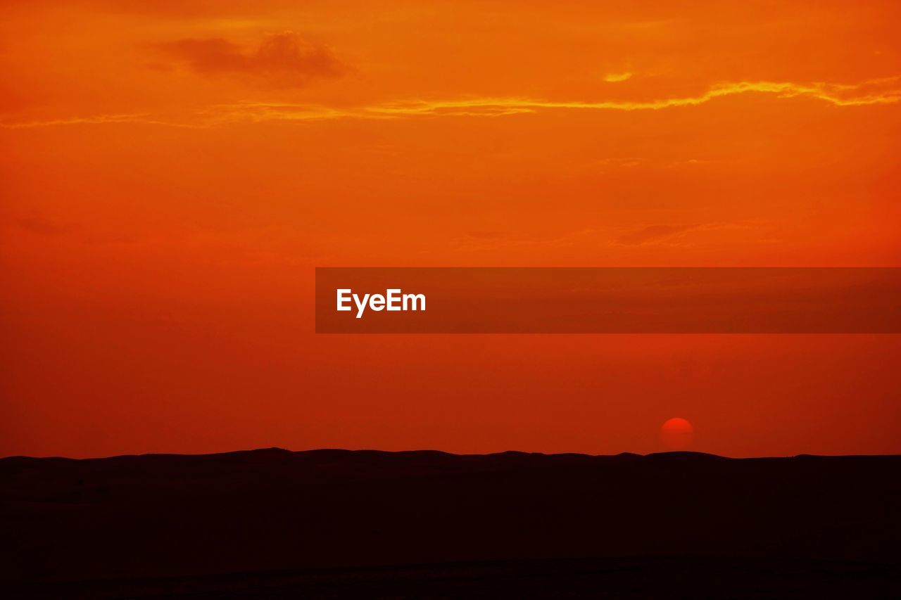 Scenic view of silhouette desert against orange sky