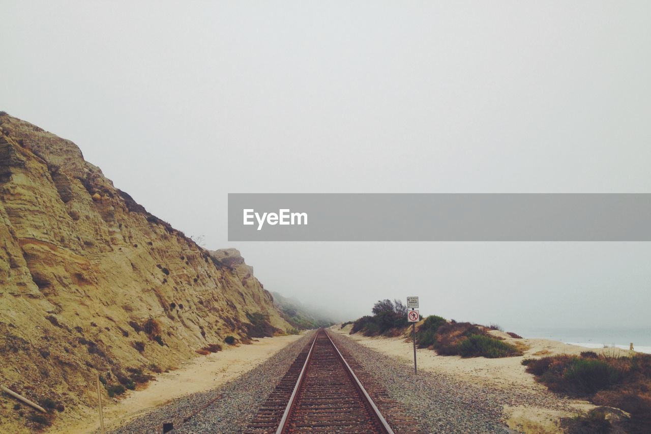 RAILROAD TRACKS AMIDST MOUNTAINS AGAINST CLEAR SKY