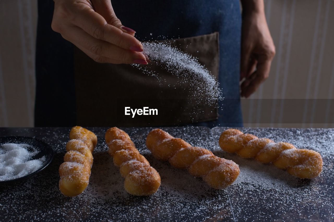 Midsection of woman sprinkling sugar on food in kitchen