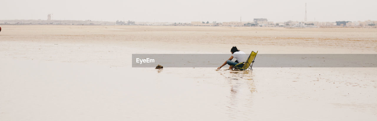 Full length of woman sitting on beach against sky