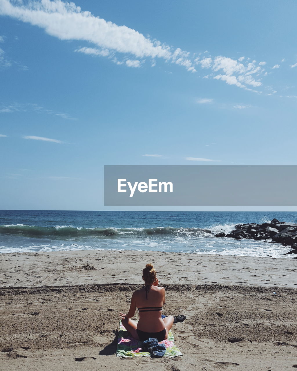 Woman sitting on beach by sea against sky