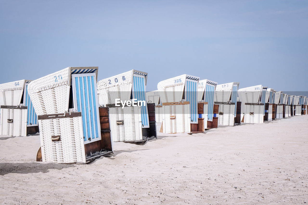 Hooded chairs at sandy beach against clear sky