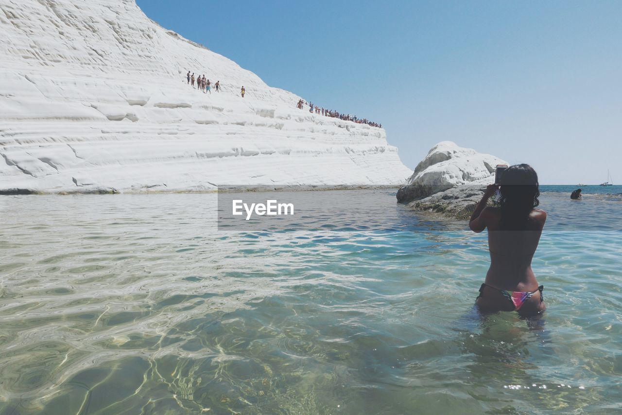 Rear view of woman in sea taking photo with smartphone