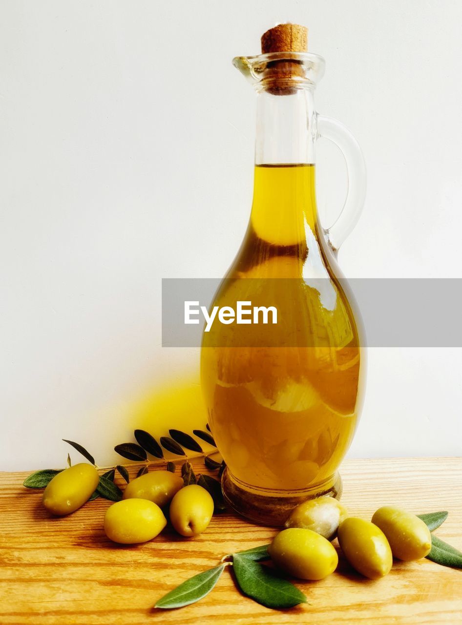Bottle containing olive oil and green olives in the background