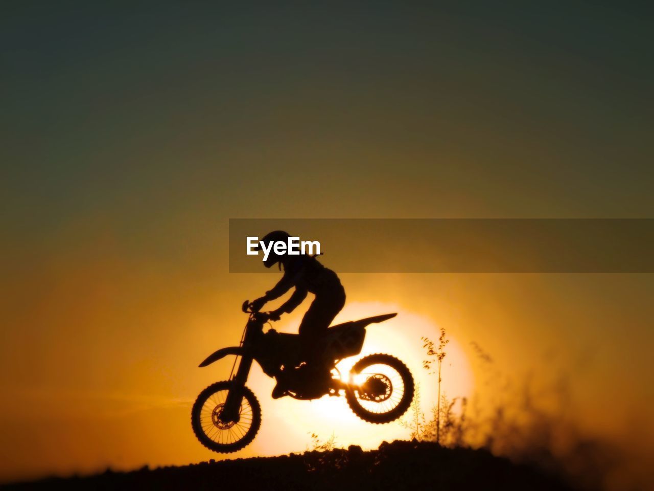 Silhouette man riding motorcycle against orange sky