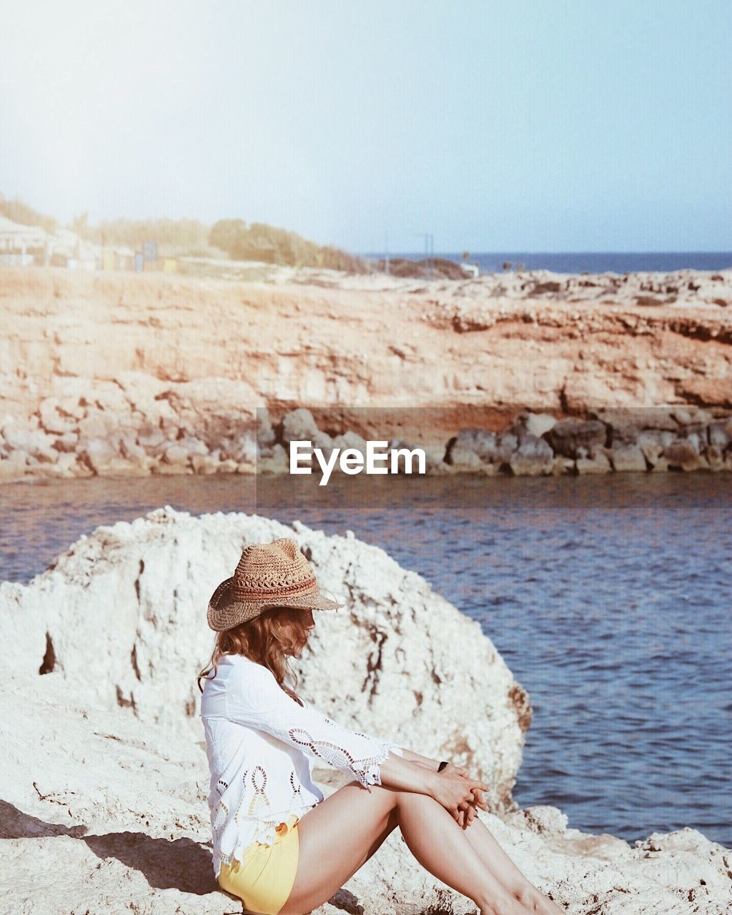 Side view of woman sitting on rock by sea against sky