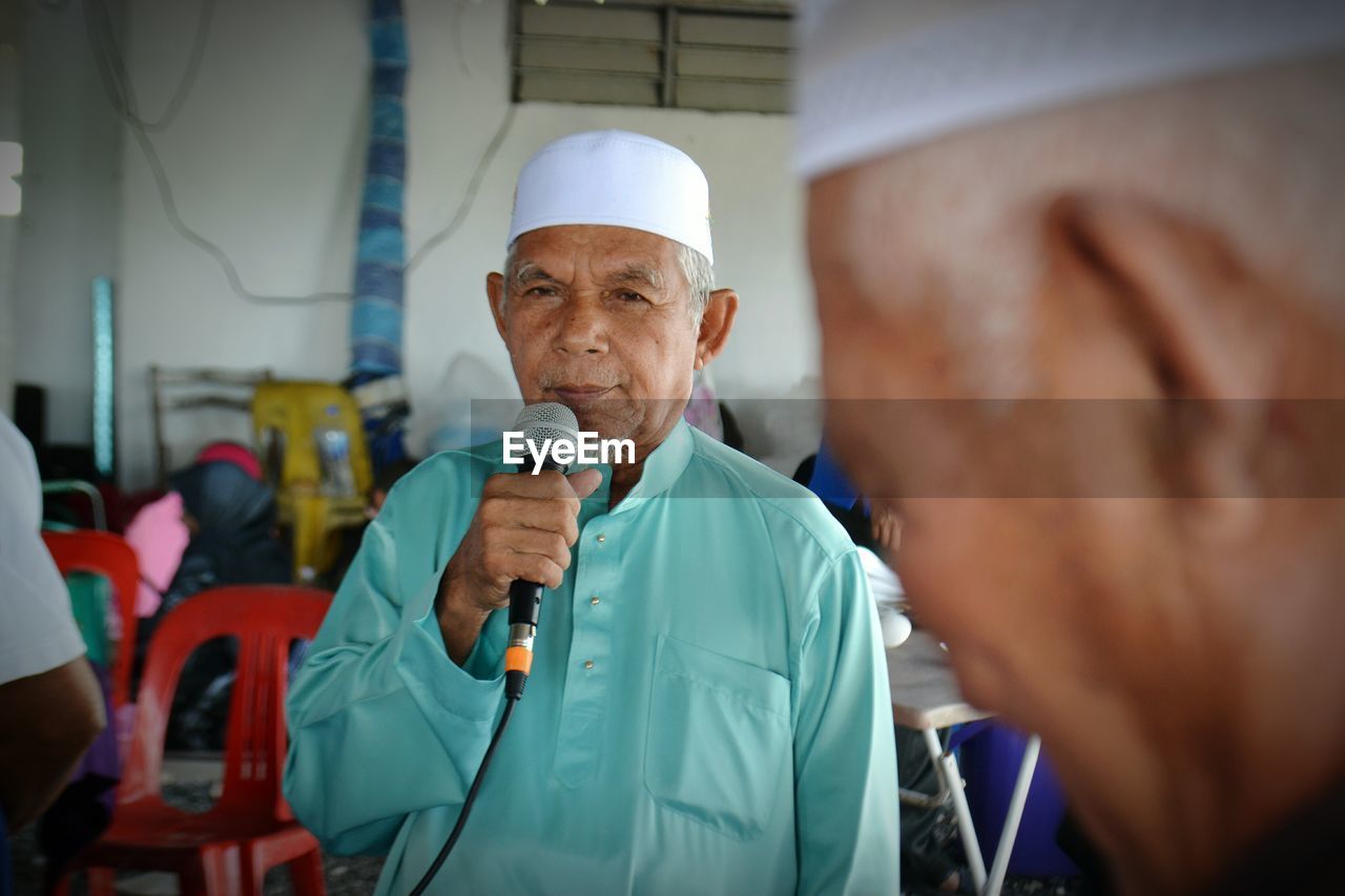 Senior man using microphone while standing indoors