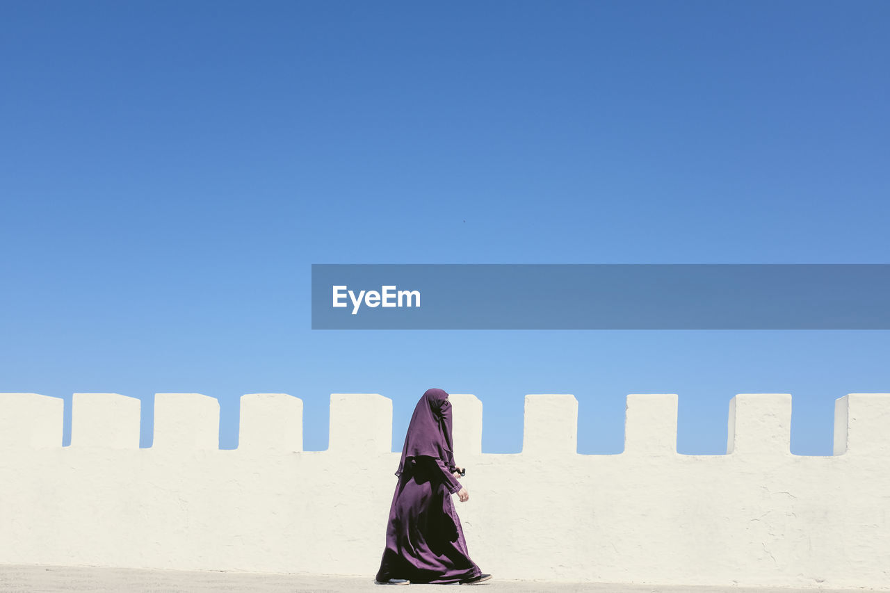 Woman with a burka walking beside a white wall