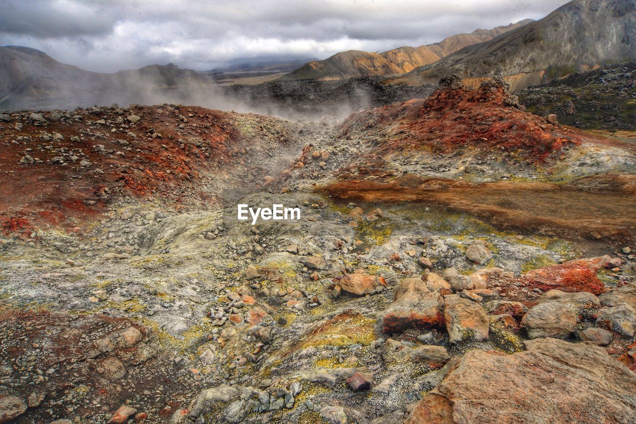 Hot springs by rock formations against cloudy sky