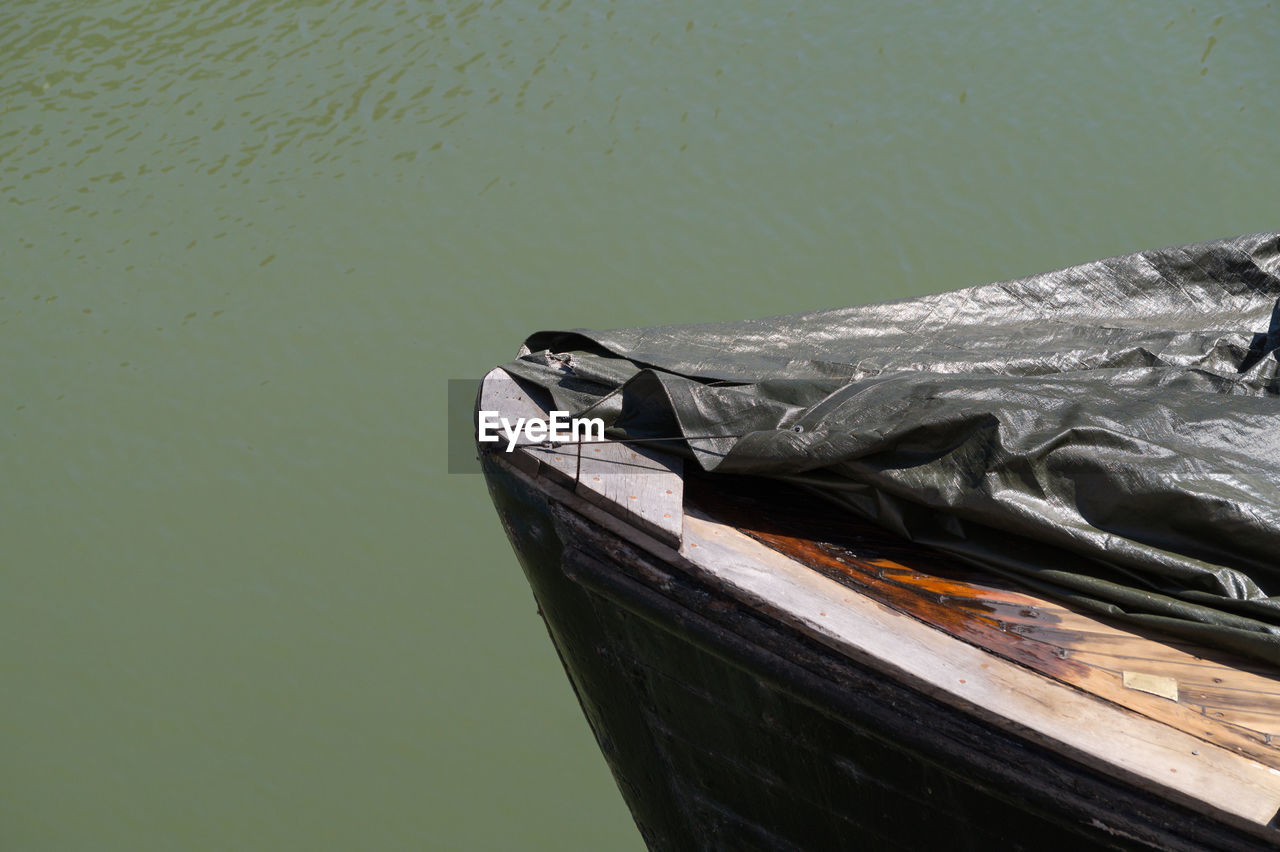 Cropped image of wooden boat covered with tarpaulin at lake