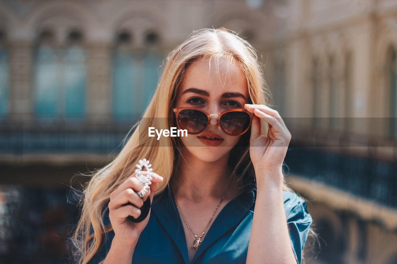 Portrait of beautiful woman wearing sunglasses against building