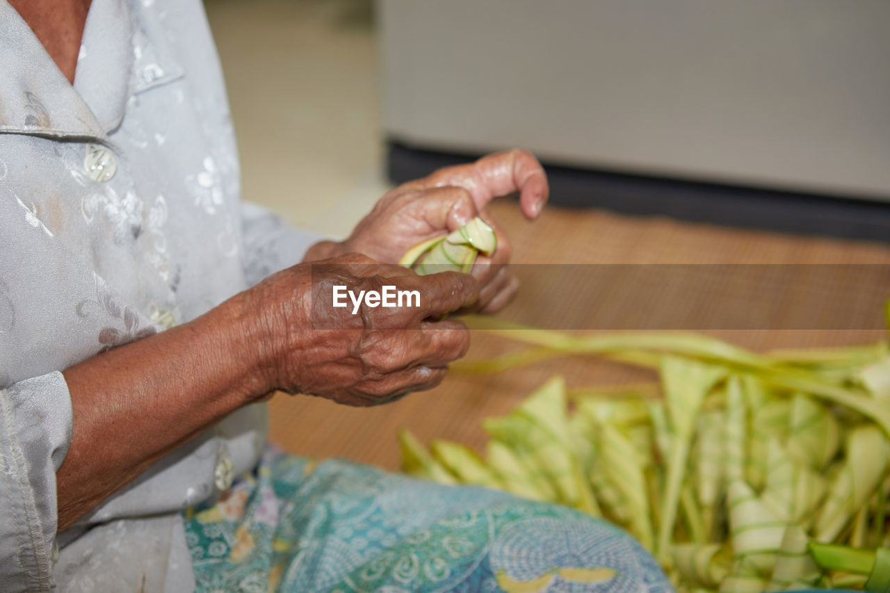 Hands of senior woman wrapping the sticky rice with palm leaf or ketupat palas