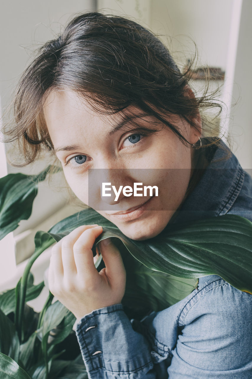 Portrait of a woman with brown hair sits on the floor of her house and hugs a plant from a pot