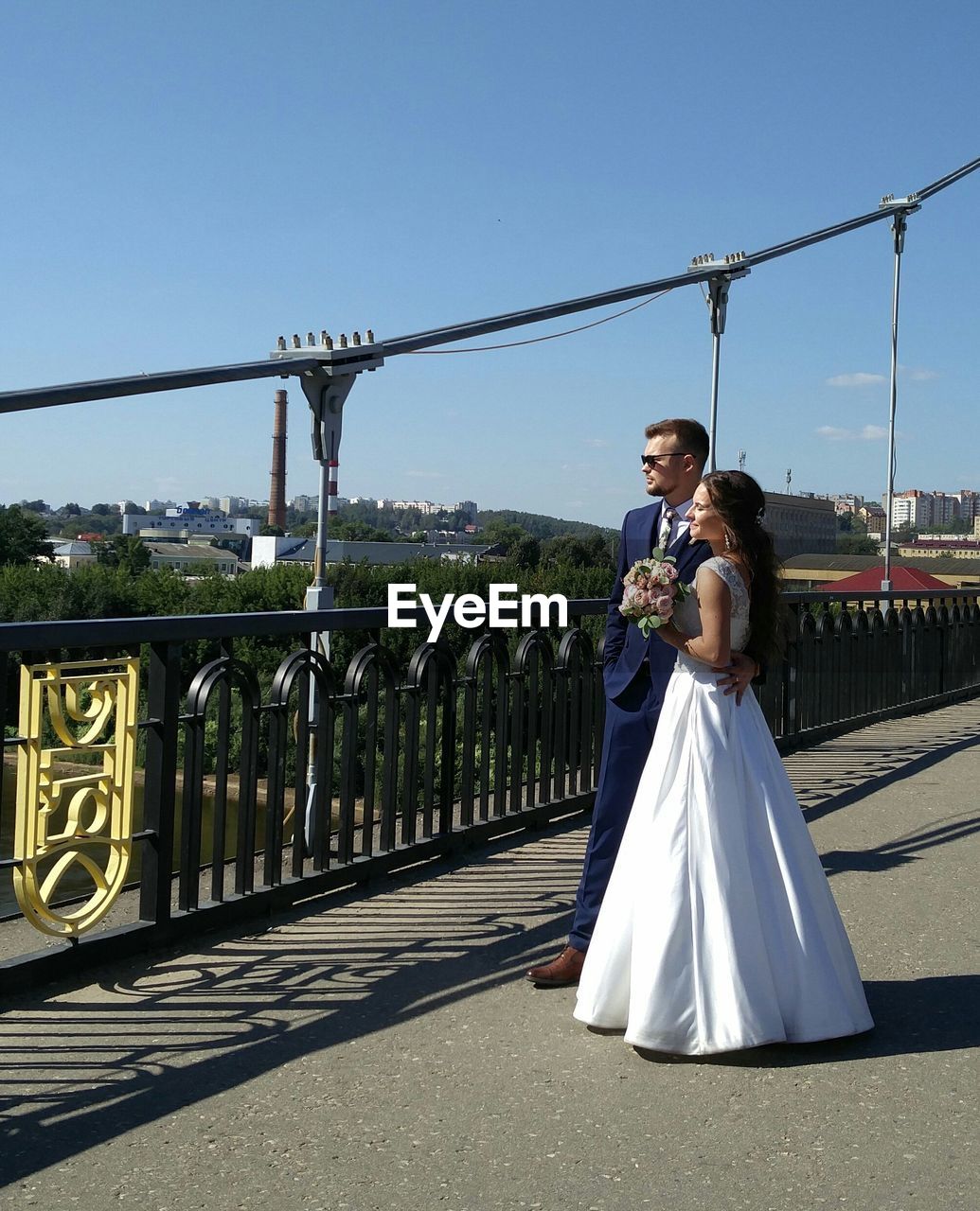 FRIENDS STANDING ON BRIDGE AGAINST SKY