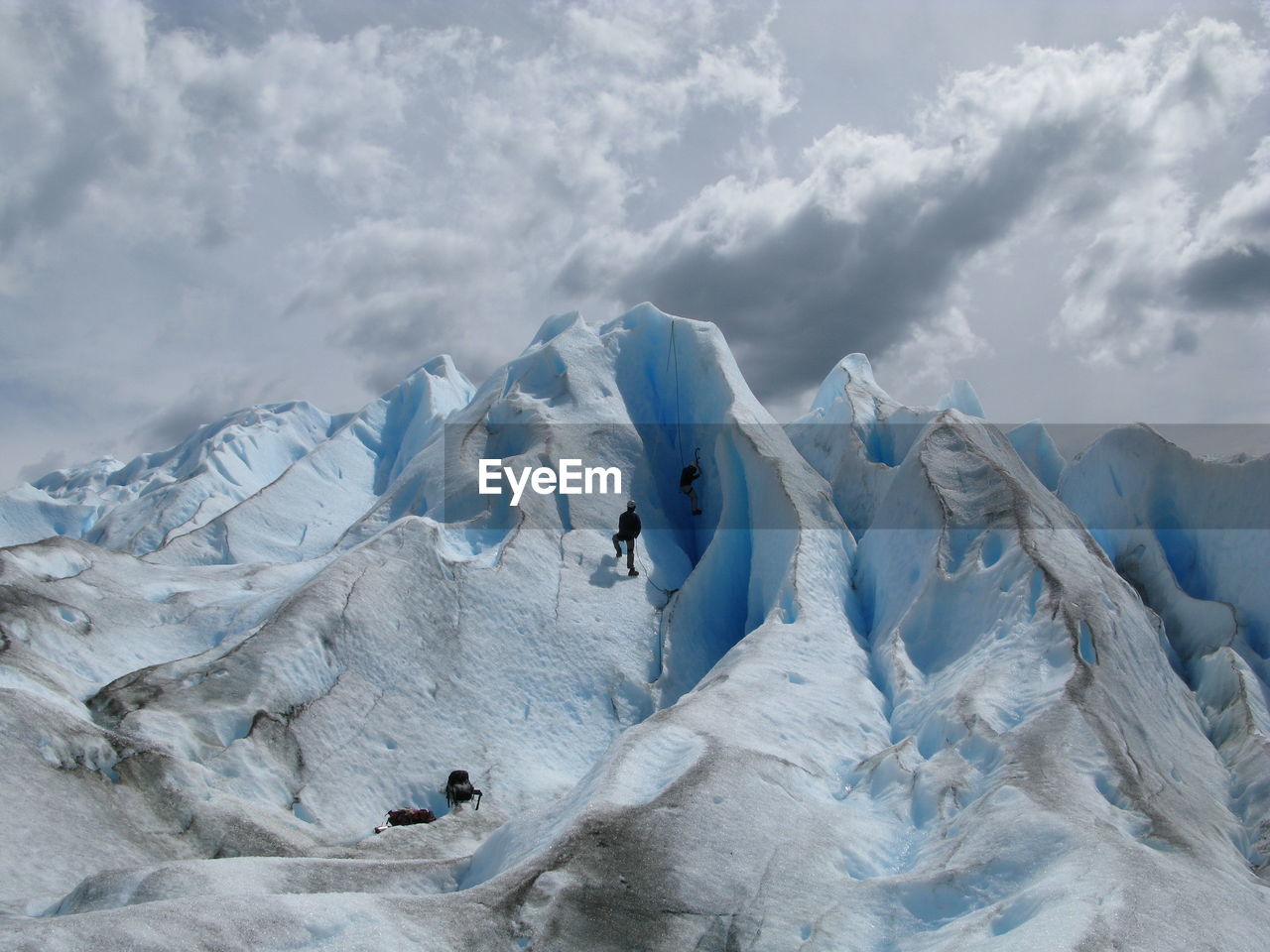 Scenic view of snowcapped mountains against sky and two people escalating them. 