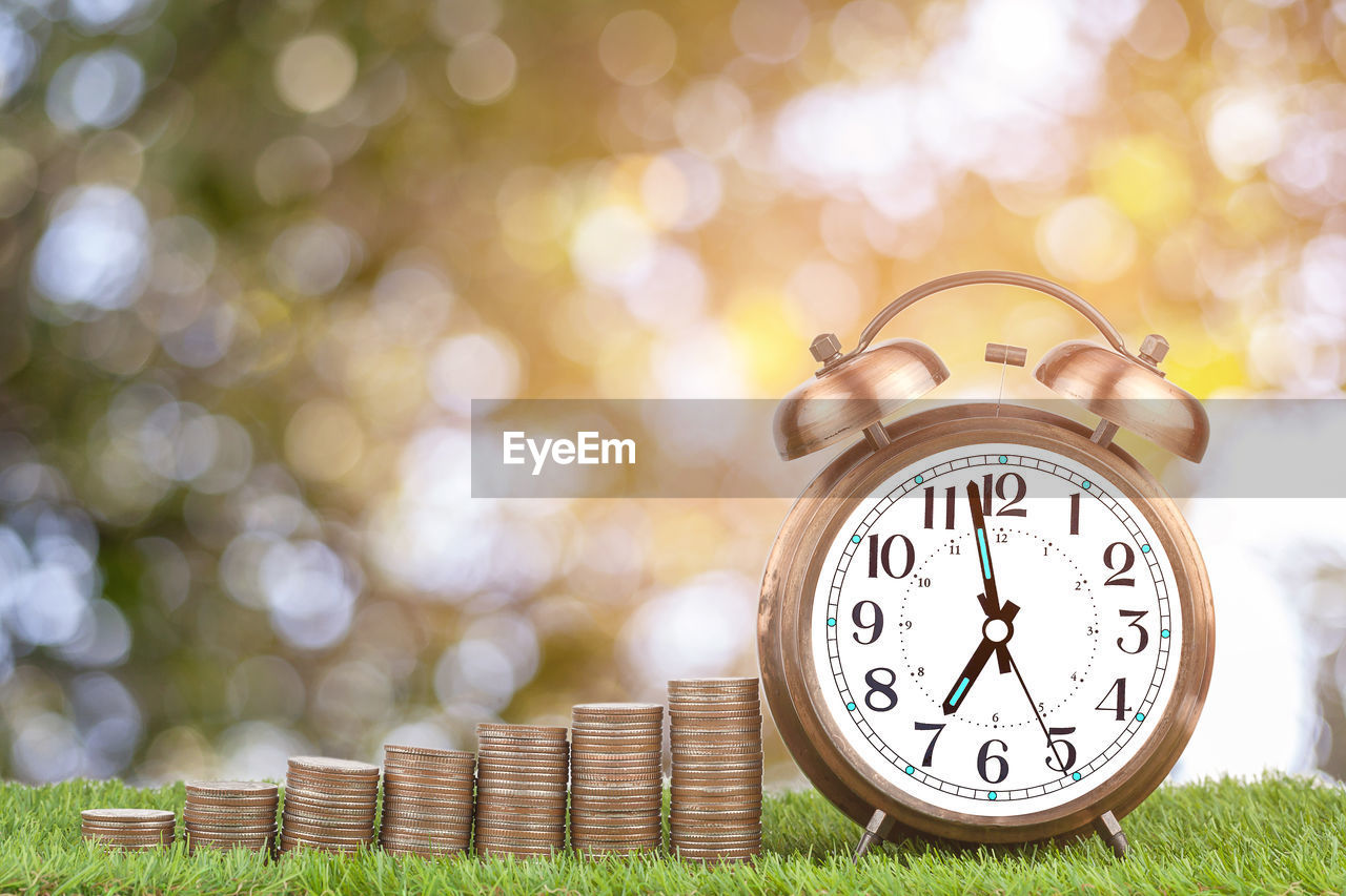 Close-up of alarm clock with coins on grassy field