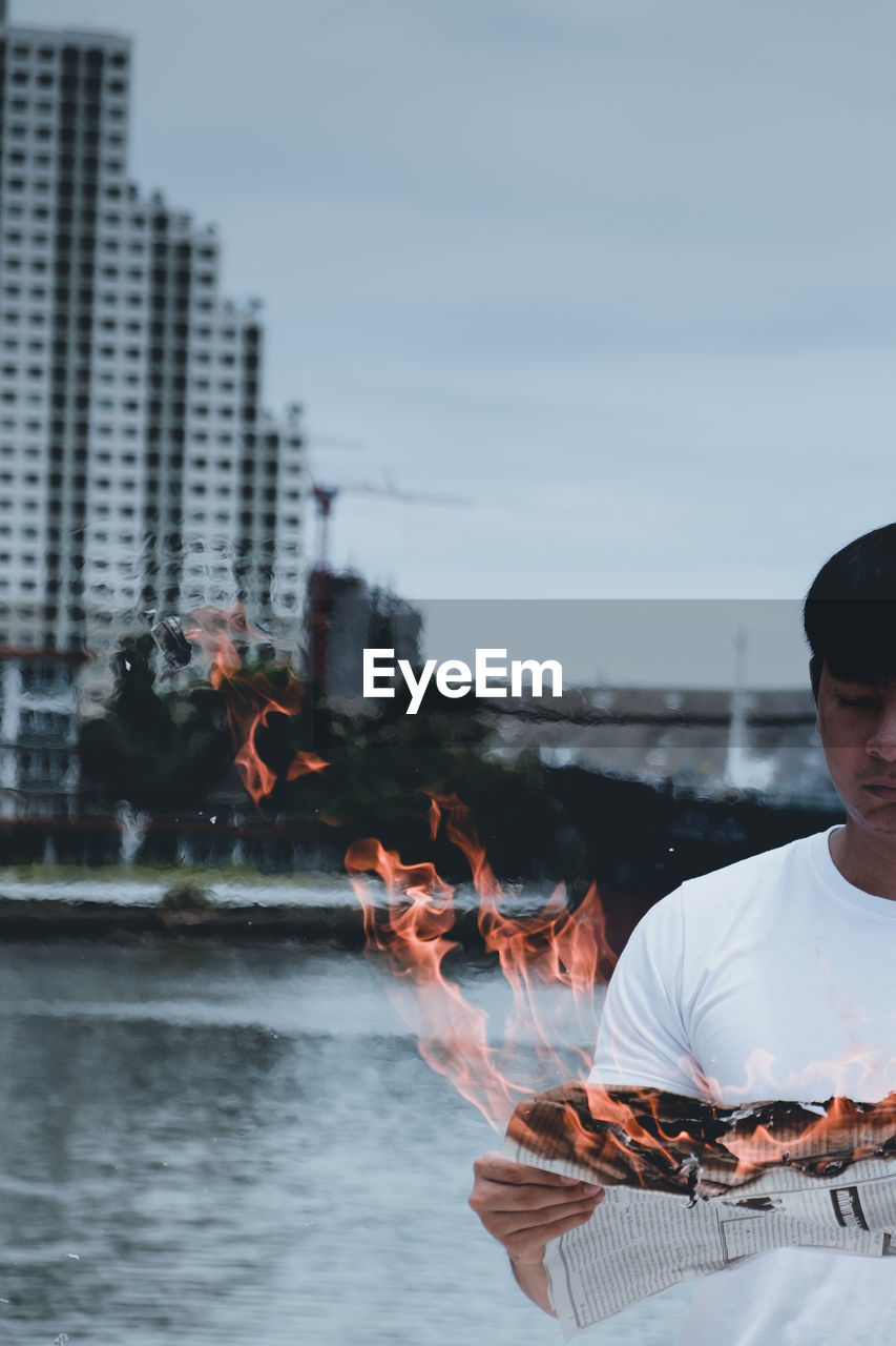 Man holding burning paper against lake and sky