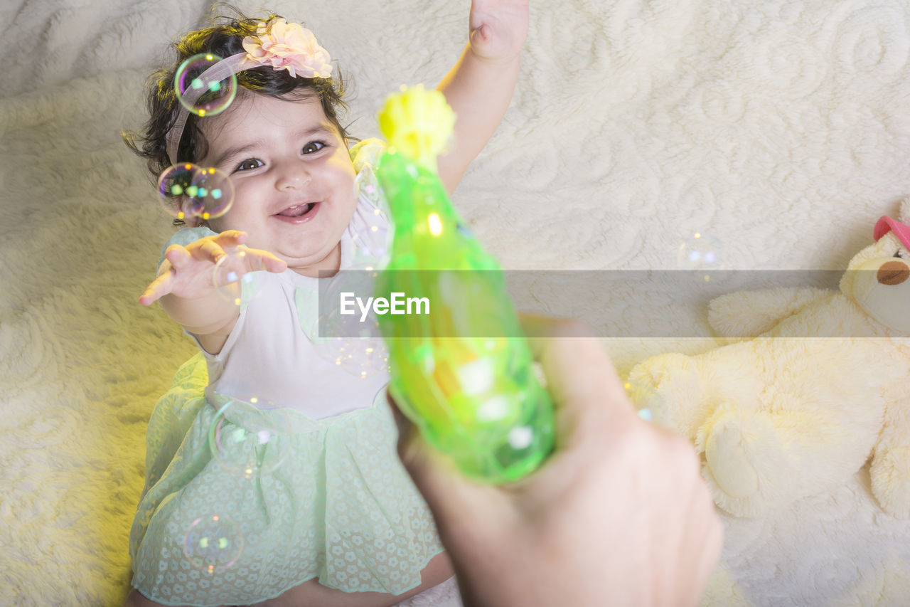 Cropped hand of person making bubbles with wand with baby girl enjoying 