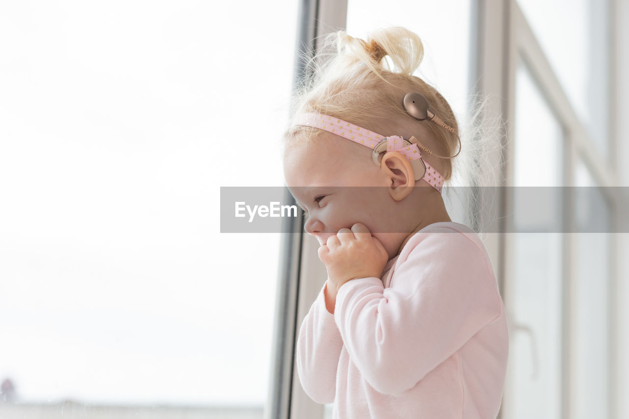 side view of young woman looking away while standing against window