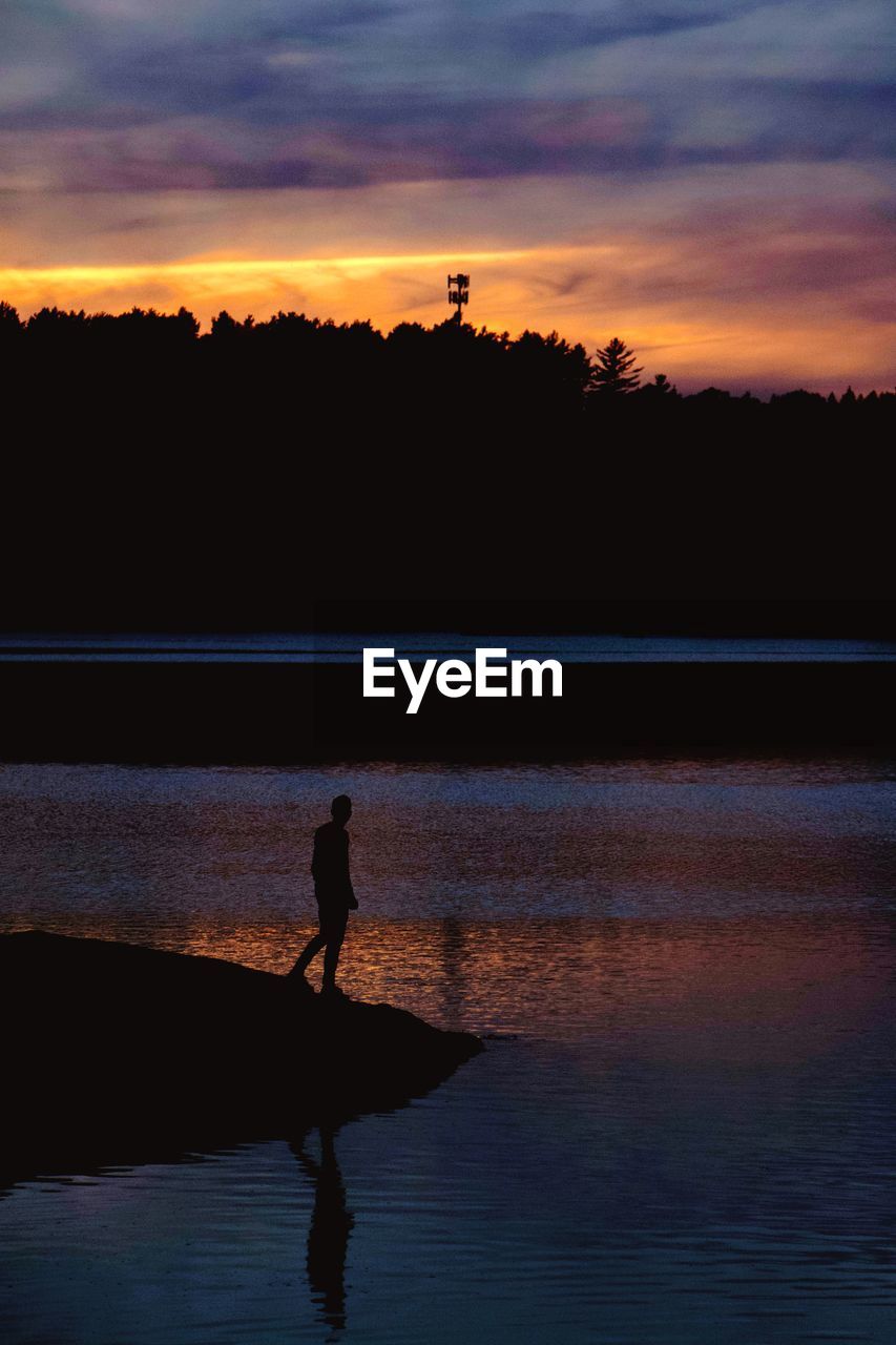 Silhouette man standing at sea against sky during sunset