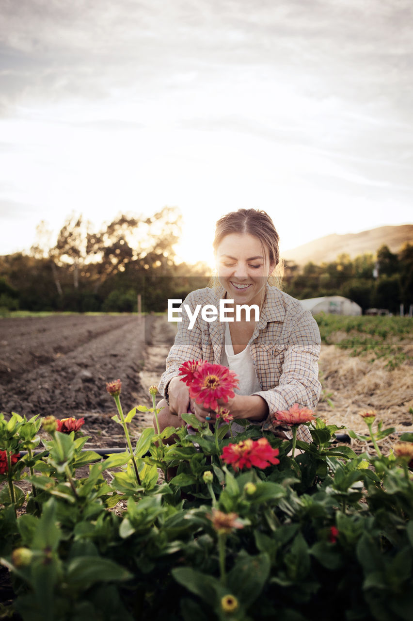 Happy female farmer working on flowering field against sky