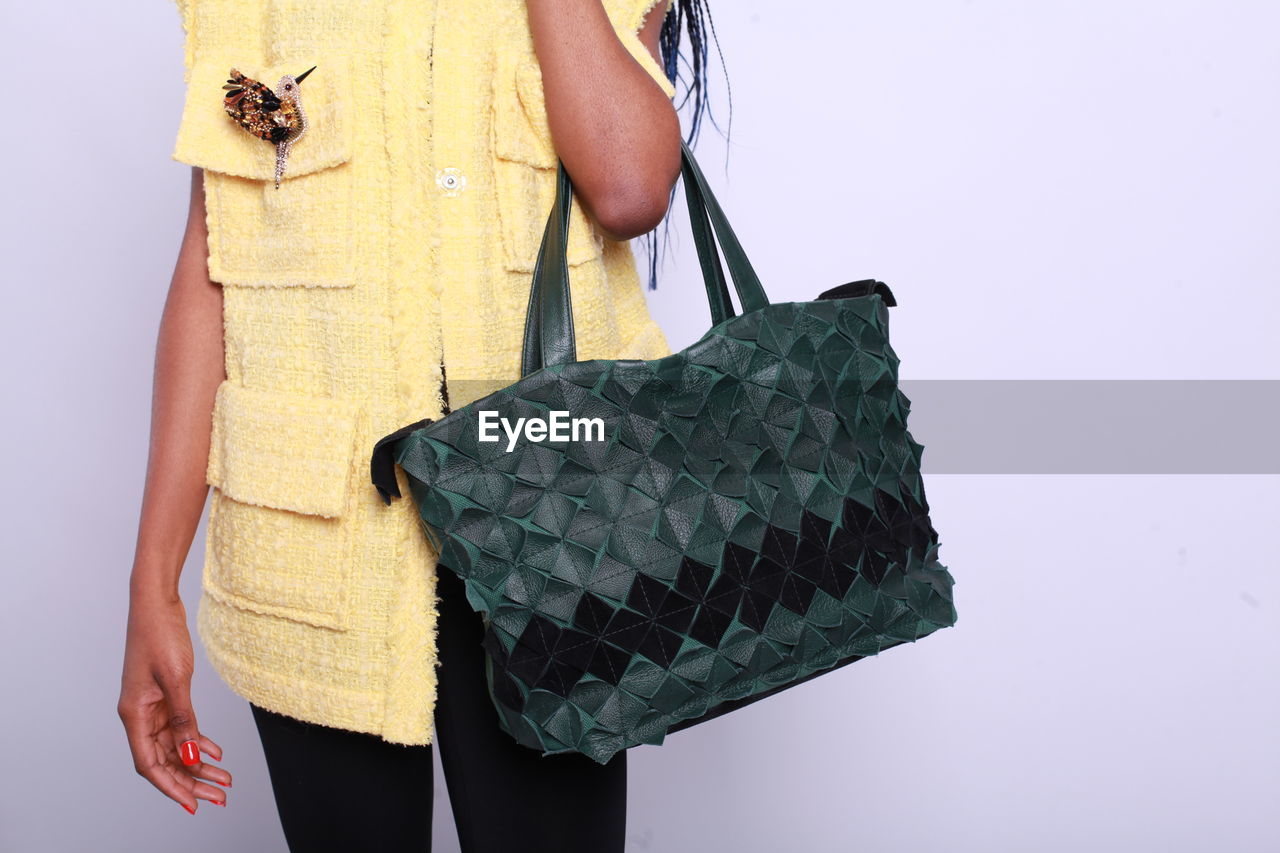 Midsection of woman holding bag against gray background