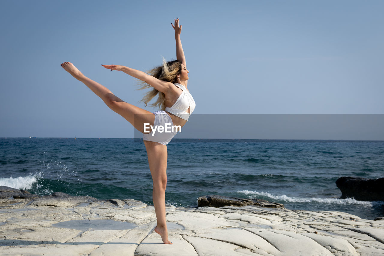 Young woman dancing outdoors on a rocky coast by the ocean