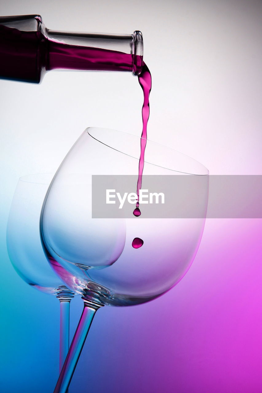 Close-up of wine pouring in wineglass against colored background