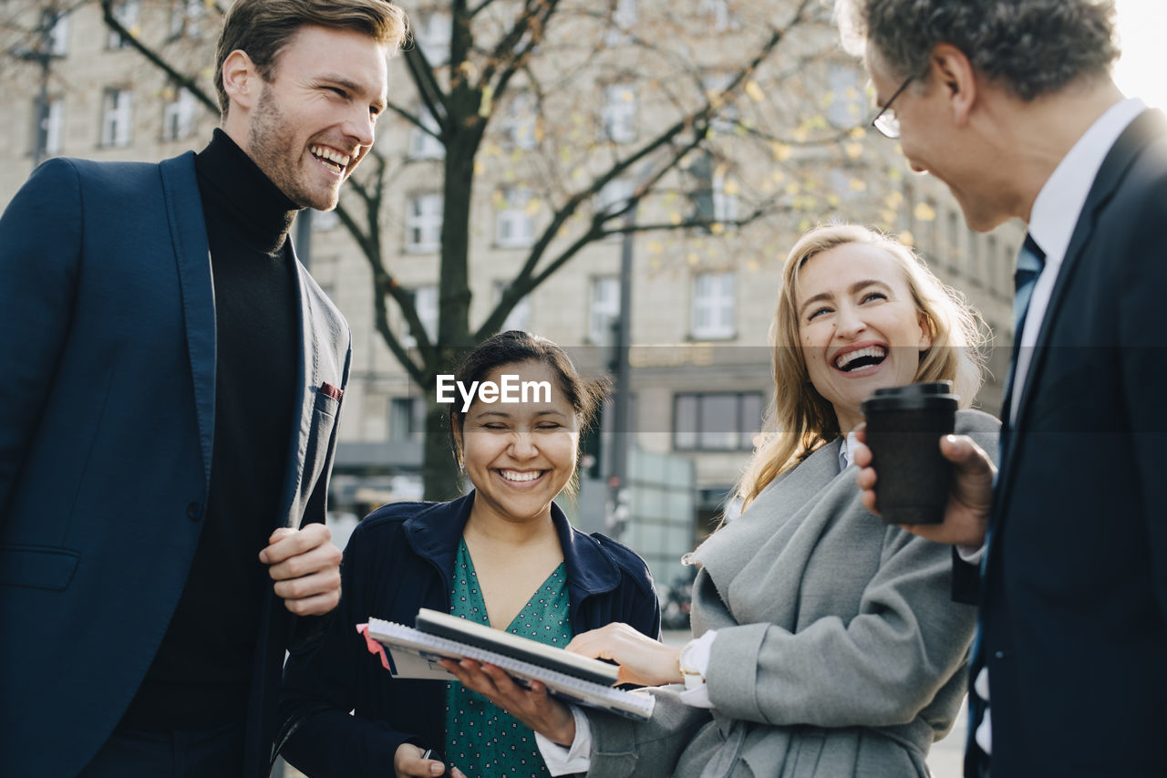 Happy business coworkers with book discussing while standing in city