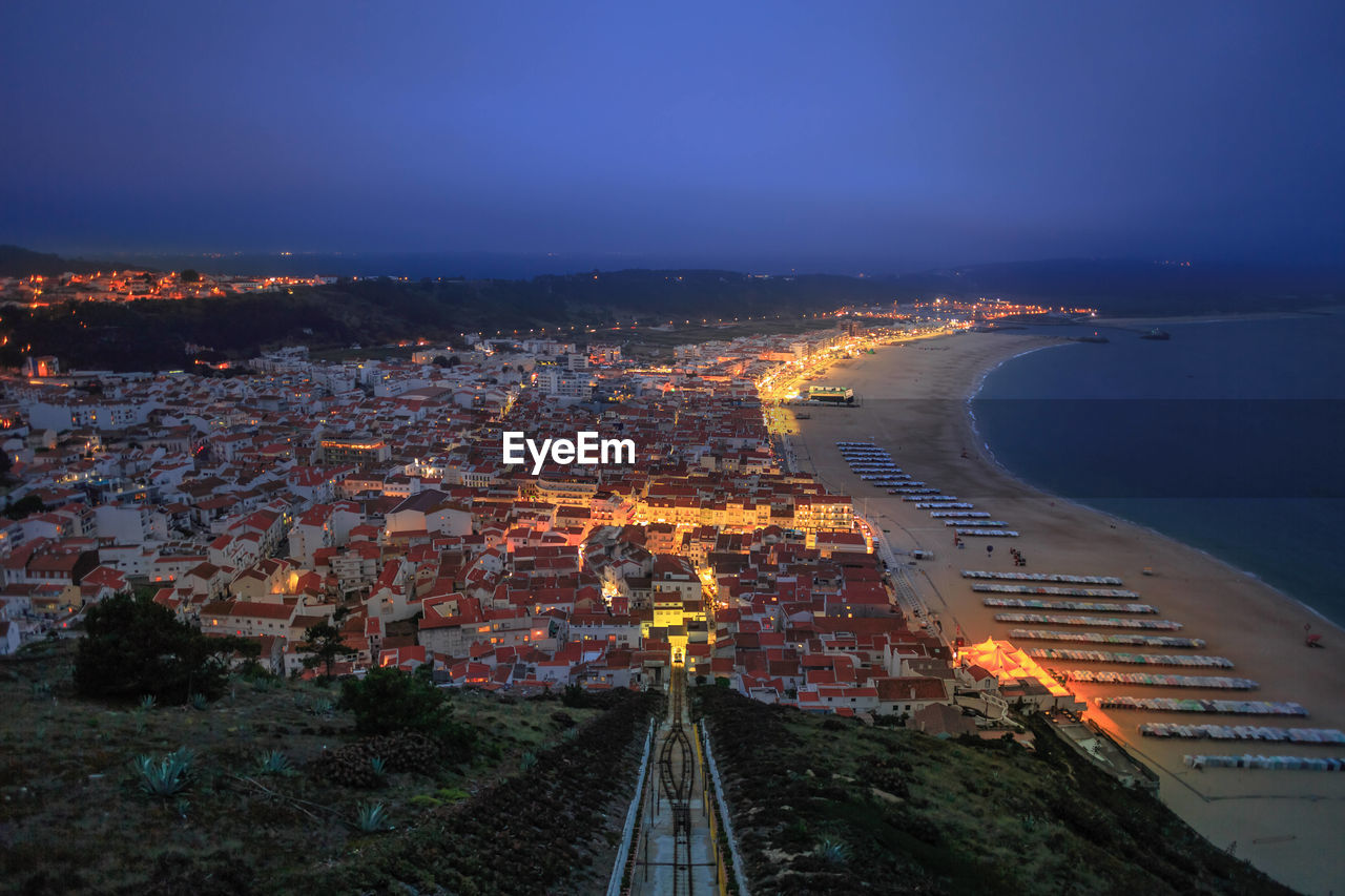 Aerial view of townscape by sea against blue sky at night