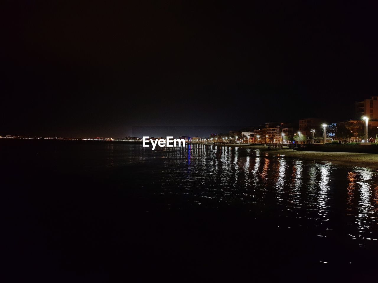 ILLUMINATED BUILDING BY SEA AGAINST SKY AT NIGHT