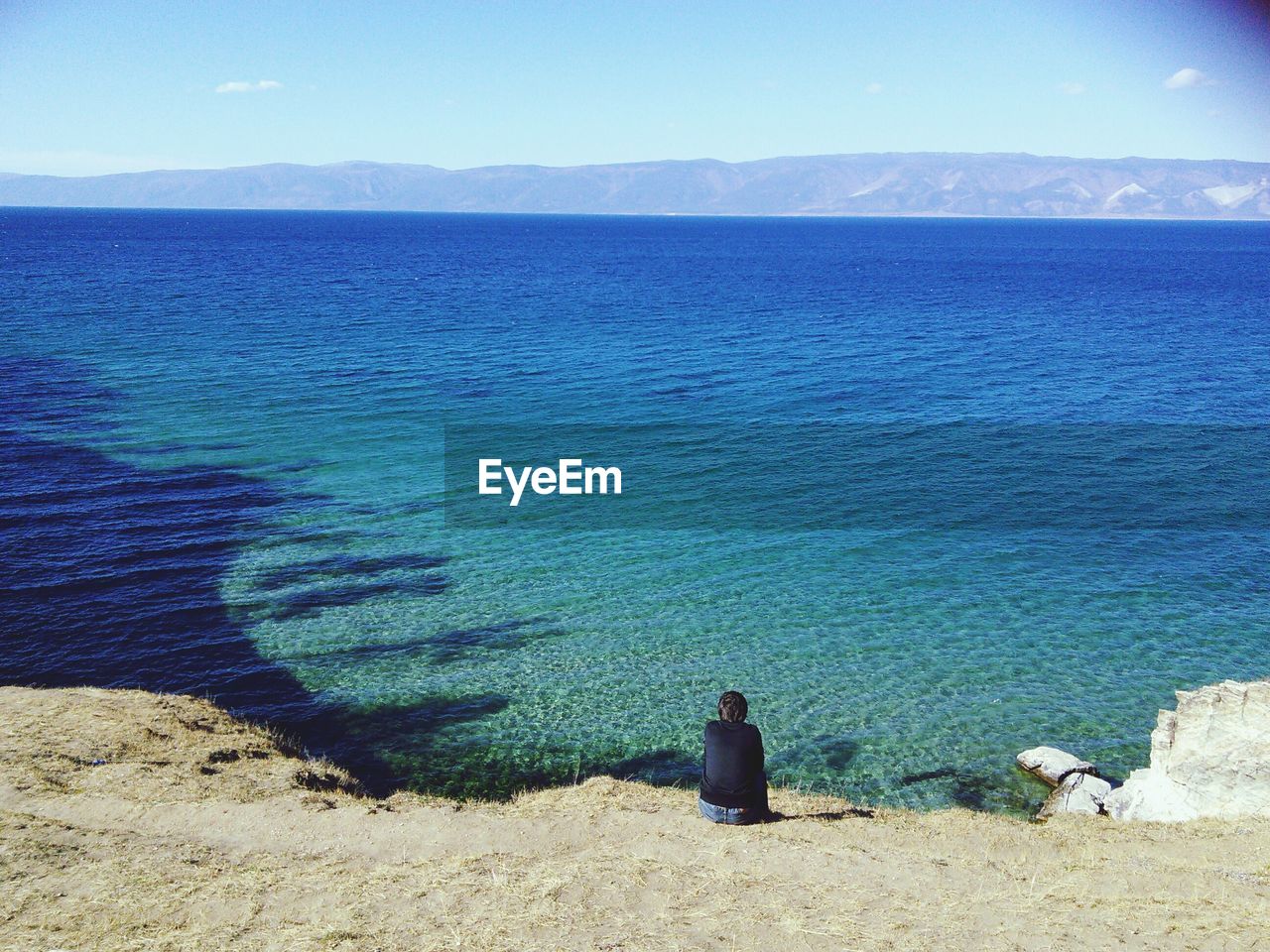 Rear view of man sitting on cliff looking at sea